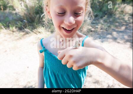 Ein Schmetterling landet auf der Hand eines jungen Mädchens, während sie in der Natur spazieren geht. Stockfoto