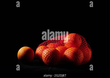 Reife Orangen in einem Netzbeutel auf schwarzem Hintergrund. Stockfoto