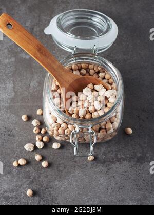 Kichererbsen in einem Glas mit einem Holzlöffel auf dunklem Grund trocknen. Stockfoto