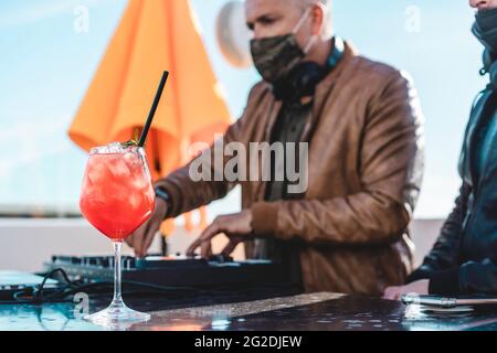 Nahaufnahme eines besonderen Cocktails bei einer Strandparty - DJ spielt Musik an der Cocktailbar im Freien mit Sicherheitsgesicht Maske für Coronavirus-Ausbruch - Entertain Stockfoto