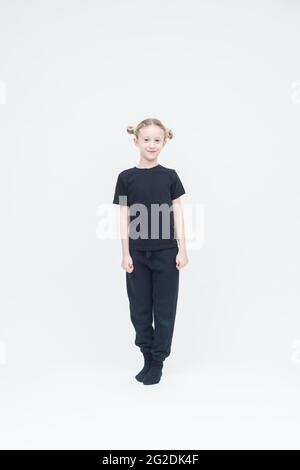 Ein Kind steht auf einem weißen nahtlosen Hintergrund und trägt ausschließlich schwarze Kleidung Stockfoto