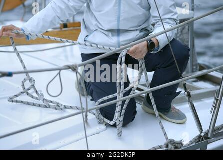 Der Segler hält Seile in den Händen und strickt einen Knoten auf einem Oberdeck der Yacht während des Festmachens. Stockfoto