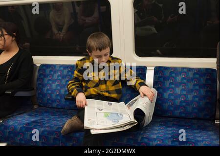 Ein Junge sitzt in einem londoner U-Bahn-Zug und liest die Zeitung. Stockfoto