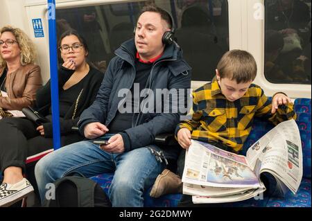 Ein Junge sitzt in einem londoner U-Bahn-Zug und liest die Zeitung. Stockfoto