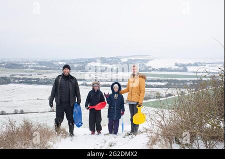 Eine Familie hat Spaß beim Rodeln auf Mill Hill in Shoreham-by-Sea, West Sussex nach einer leichten Schneedecke auf dem Boden. Stockfoto