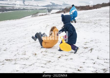 Eine Familie hat Spaß beim Rodeln auf Mill Hill in Shoreham-by-Sea, West Sussex nach einer leichten Schneedecke auf dem Boden. Stockfoto