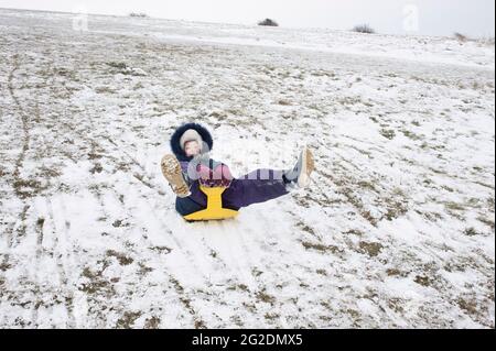 Eine Familie hat Spaß beim Rodeln auf Mill Hill in Shoreham-by-Sea, West Sussex nach einer leichten Schneedecke auf dem Boden. Stockfoto