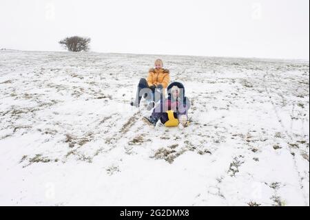 Eine Familie hat Spaß beim Rodeln auf Mill Hill in Shoreham-by-Sea, West Sussex nach einer leichten Schneedecke auf dem Boden. Stockfoto