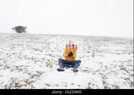 Eine Familie hat Spaß beim Rodeln auf Mill Hill in Shoreham-by-Sea, West Sussex nach einer leichten Schneedecke auf dem Boden. Stockfoto