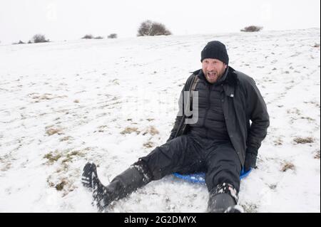 Eine Familie hat Spaß beim Rodeln auf Mill Hill in Shoreham-by-Sea, West Sussex nach einer leichten Schneedecke auf dem Boden. Stockfoto