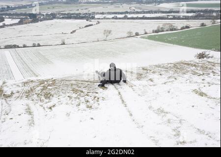 Eine Familie hat Spaß beim Rodeln auf Mill Hill in Shoreham-by-Sea, West Sussex nach einer leichten Schneedecke auf dem Boden. Stockfoto