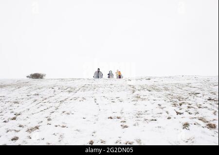 Eine Familie hat Spaß beim Rodeln auf Mill Hill in Shoreham-by-Sea, West Sussex nach einer leichten Schneedecke auf dem Boden. Stockfoto