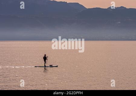 Ein Mann auf seinem Stehpaddel auf dem Genfer See bei Sonnenuntergang. Stockfoto