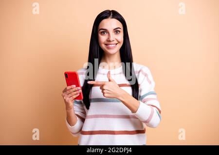 Foto von jungen glücklich positiv fröhlich lächelnd Mädchen zeigen Finger auf Telefon-Werbung isoliert auf beige Farbe Hintergrund Stockfoto