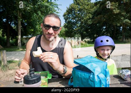 Eine Familie, die auf einer Fahrradtour auf einer Bank in Frankreich ein Lunchpaket isst. Stockfoto