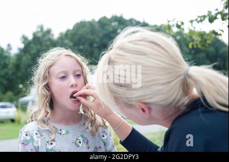 Ein junges Mädchen hat ihren ersten Zahn von ihrer Mutter herausgezogen. Stockfoto