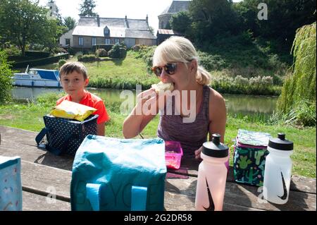 Eine Familie, die auf einer Fahrradtour auf einer Bank in Frankreich ein Lunchpaket isst. Stockfoto