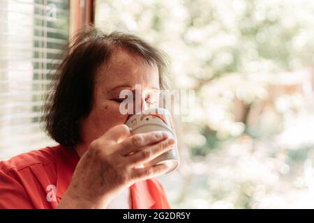 Ältere Frau, die morgens Kaffee am Fenster trinkt. Speicherplatz kopieren Stockfoto