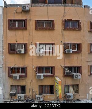 Aqaba, Jordanien - 21. Januar 2020: Klimaanlagen mit großen Ventilatoren an der Fassade eines alten Gebäudes in der Nähe von Fenstern, viele unordentliche Kabel in der Nähe, Stockfoto