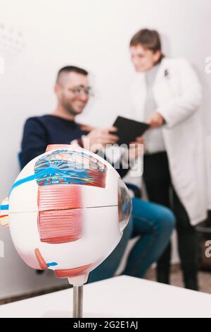 Ein Optiker-Patient folgt den Anweisungen eines Optiker, um während einer Visionsgraduierung eine Lesetabelle zu lesen. Sie sind im Hintergrund nicht fokussiert, Stockfoto