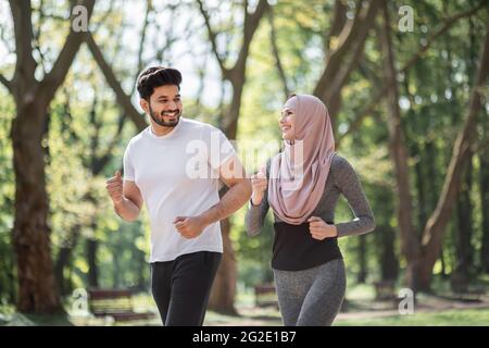 Gesundes Sportpaar in aktiver Kleidung genießen Morgenlauf im grünen Park. Muslimischer Mann und Frau in Hijab, die Freizeit zum Training an der frischen Luft verbringen. Stockfoto