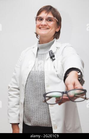 Der Mitarbeiter eines Optikers gibt einem Kunden eine neue Brille, die er in der ersten Person sieht. Die Brille ist unscharf und das Gesicht des Optometristen ist fokussiert. Stockfoto