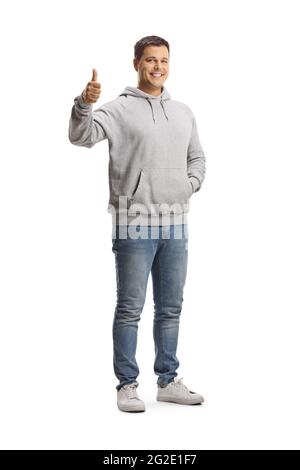 In voller Länge Porträt eines jungen Mannes in einem grauen Hoodie und Jeans zeigt Daumen nach oben isoliert auf weißem Hintergrund Stockfoto