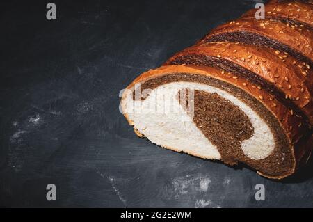 Ungewöhnlicher zweifarbiger frischer Laib Brot auf schwarzem Hintergrund, Foto in einer niedrigen Taste bei hartem Licht, Nahaufnahme Stockfoto