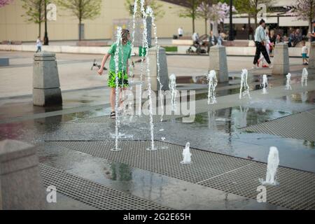 Stadtbrunnen auf dem Platz. Wasser sprudelt aus den Gehwegen. Flugzeugbrunnen in der Stadt. Spritzende Wasserspiele. Stockfoto