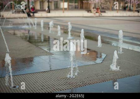 Stadtbrunnen auf dem Platz. Wasser sprudelt aus den Gehwegen. Flugzeugbrunnen in der Stadt. Spritzende Wasserspiele. Stockfoto