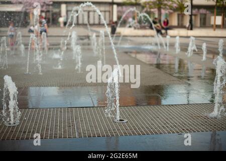 Stadtbrunnen auf dem Platz. Wasser sprudelt aus den Gehwegen. Flugzeugbrunnen in der Stadt. Spritzende Wasserspiele. Stockfoto