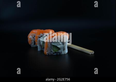 Nahaufnahme von drei diagonal angeordneten Sushi-Stücken mit Essstäbchen auf einem isolierten schwarzen Hintergrund. Stockfoto