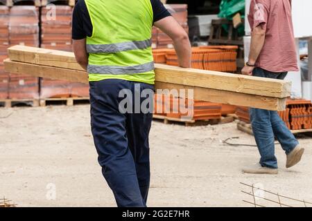 Rückansicht eines unbekannten Bauarbeiters, der Holz im Lager oder auf der Baustelle hält und trägt Stockfoto