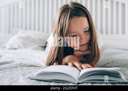 Hübsches Mädchen 8-9 Jahre alt liegt auf dem Bett und liest das Buch. Komfort, gemütliches Zuhause Konzept. Lifestyle. Stockfoto