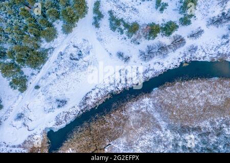Ländliche Landschaft im Winter. Blick von oben auf den bewaldeten Bach entlang des Pinienwaldes. Natur Hintergrund Stockfoto