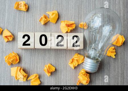 2022 Text Holzwürfelblöcke und zerknittertes Papier mit Glühbirne auf Holztisch Hintergrund. Neues Jahr Neue Ideen, Kreativ, Innovation, Phantasie, inspir Stockfoto