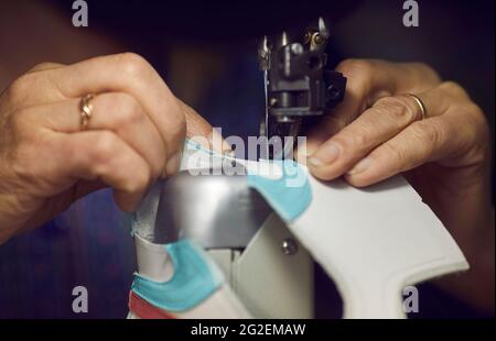 Schuhfabrikarbeiter, der mit einer Nähmaschine Details für neue Leder-Sneakers macht Stockfoto