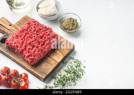 Rohes Hackfleisch mit Gewürzen, Gemüse und Kräutern und Fleischbällchen, auf weißem Stein-Hintergrund, mit Platz für Text Stockfoto