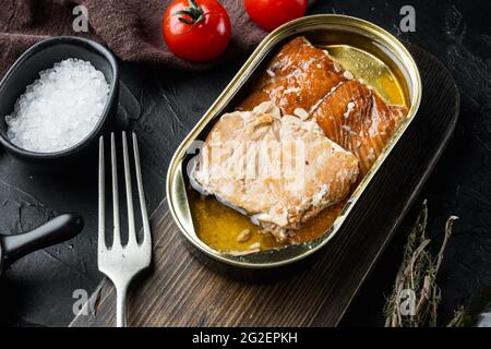 Set aus geräuchertem Fisch aus der Dose mit wildem rosafarbenem Lachs, auf Holzschneidebrett, auf schwarzem Hintergrund mit Kräutern und Zutaten Stockfoto