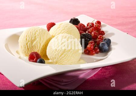 Drei Kugeln Vanilleeis und verschiedene Beerenfrüchte auf weißem Teller Stockfoto