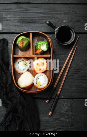 Hausgemachte Sushi Bento Box mit Sushi Rolls Set, auf schwarzem Holztisch Hintergrund, Draufsicht flach liegend Stockfoto