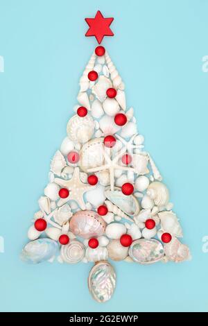 Alternative Weihnachtsbaum-Design mit Muscheln und roten Kugel-Kugel-Dekorationen auf blauem Hintergrund. Abstraktes Konzept Weihnachten. Stockfoto