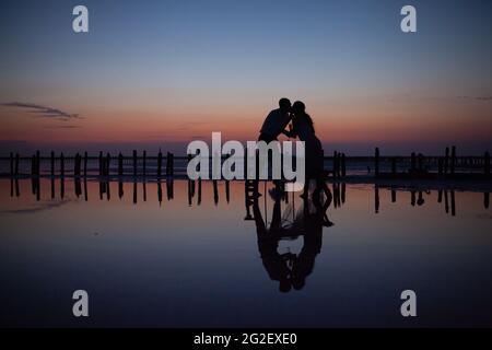 Liebevolles Hochzeitspaar bei Sonnenuntergang am rosa See Stockfoto