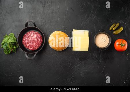 Zutaten zum Kochen von Burgern. Hacksteaks, Brötchen, Tomaten, Kräuter und Gewürze Set, auf schwarzem Steingrund, Draufsicht flach liegend, mit Kopie sp Stockfoto