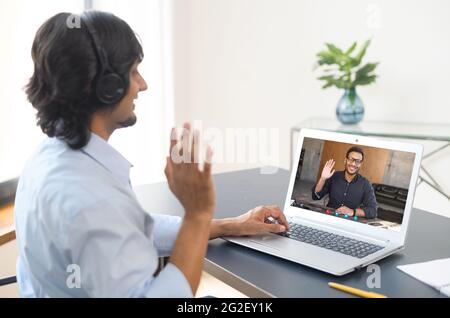 Zwei indische männliche Büroangestellte begrüssen sich gegenseitig, sprechen online über Video Connect auf einem Laptop, Geschäftspartner diskutieren Aufgaben, Männer Kollegen, die an Videotreffen auf Distanz beteiligt sind. Videoanruf Stockfoto