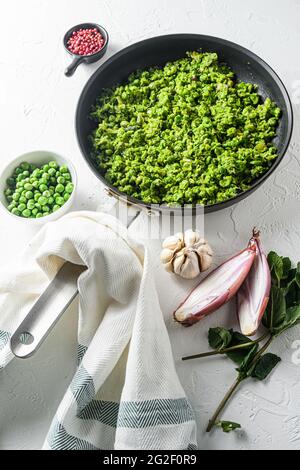 Hausgemachte Muscherbsen gekochte Bratpfanne und Erbsen in einer Schüssel mit Minze Schalotte Pfeffer und Salz Seitenansicht über weiße Steinoberfläche Bio-Keto Lebensmittel aus nächster Nähe Stockfoto