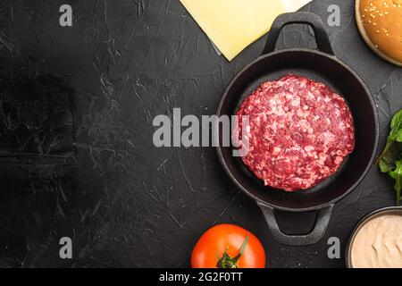 Hausgemachter Hamburger. Hacksteaks, Sesambrötchen mit anderen Zutaten, auf schwarzem Stein-Hintergrund, Draufsicht flach, mit Platz für Text Stockfoto