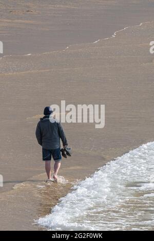 Ein Mann, der allein am Fistral Beach in Newquay in Cornwall entlang der Küste läuft. Stockfoto