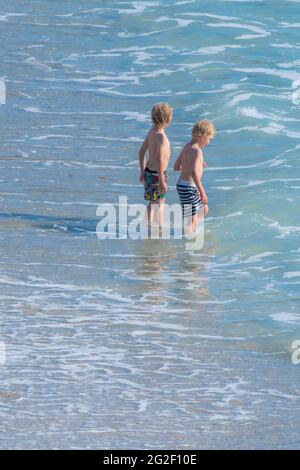Zwei kleine Jungen stehen im Meer zusammen bei strahlendem Sommersonnenschein. Stockfoto
