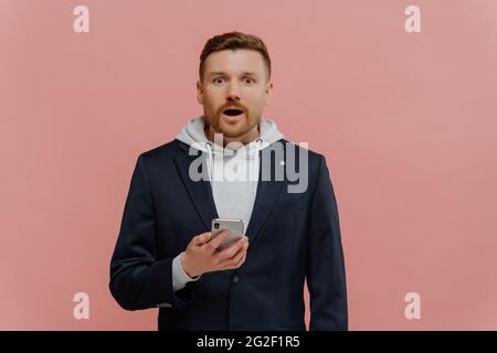 Junger aufgeregt Mann hält Smartphone und Blick auf die Kamera mit überraschter Gesichtsausdruck Stockfoto